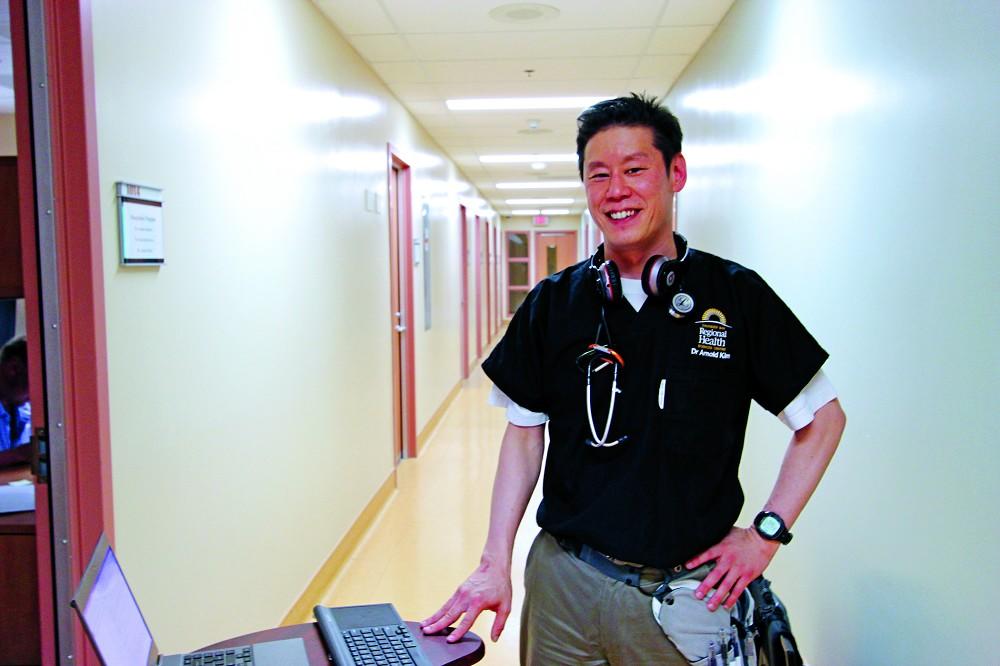 Dr. Arnold Kim standing in a hallway with a laptop